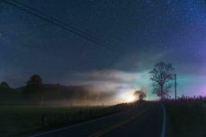 Lights from a house are illuminated in fog that blankets the road ahead under a starry sky in rural West Virginia